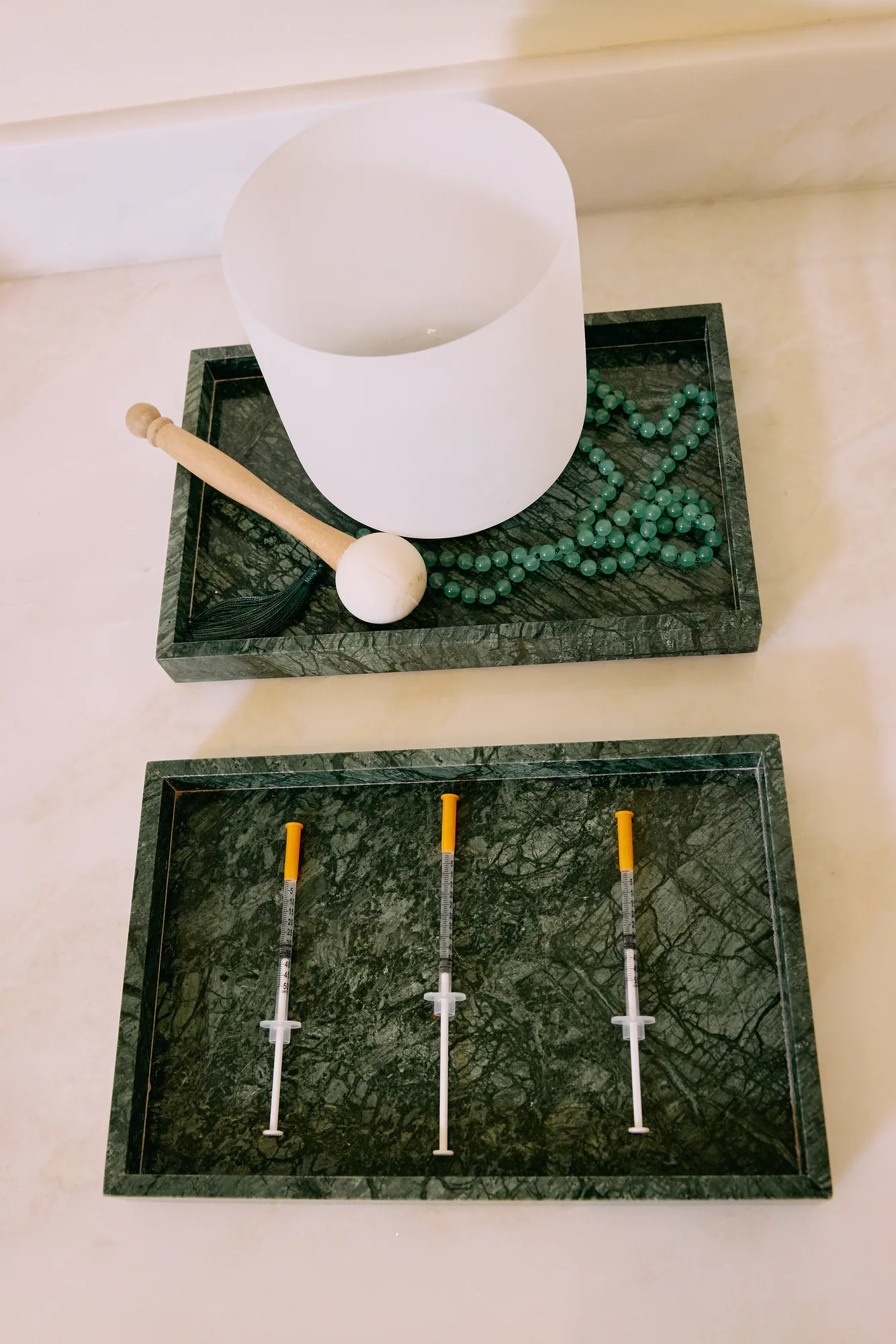 White singing bowl, green beads, and capped syringes arranged on green stone trays