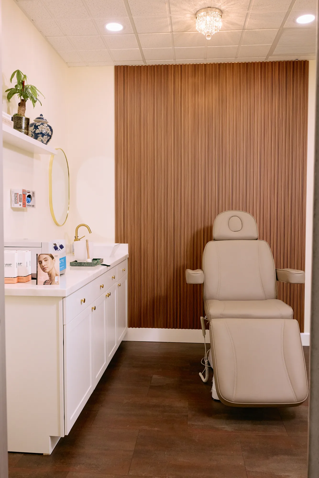 Treatment chair against a wood-panel wall with cream cabinetry and a round mirror